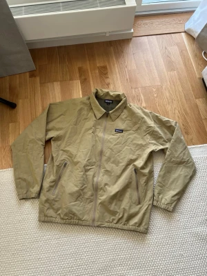 Patagonia jacka - Säljer denna Patagonia M’S baggies jacket i färgen classic tan. Jackan är endast testad en gång! Perfekt jacka inför våren. Med vind och vattenavvisande material. Nypris 1799kr Mått:  Axel-Axel 53cm Armhåla-Armhåla 65cm Längd 70cm