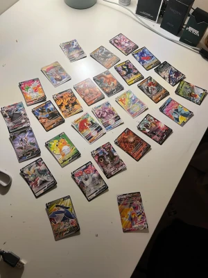 Samling Pokémonkort V-kort - Stor samling Pokémonkort med flera V-kort och färgstarka motiv. Korten har olika Pokémon med unika illustrationer och holografiska effekter. Perfekt för samlare eller dig som vill utöka din lek med coola och sällsynta kort.