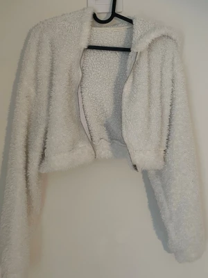 Vit croppad teddykofta med luva -  vit teddyjacka i croppad modell med dragkedja framtill och luva. 