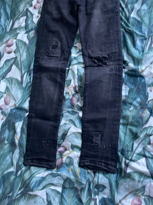 Svarta jeans från Dsquared2 - Säljer ett par svarta jeans från Dsquared2 med slitningar och trasiga detaljer på benen. Jeansen har en klassisk femficksmodell. Snygga att matcha med sneakers eller boots.