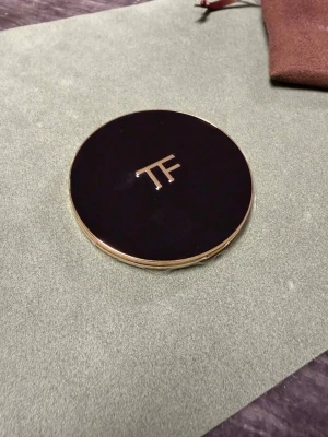Tom Ford  kompakt - Lyxig  i kompaktformat från Tom Ford. Svart rund dosa med guldfärgade detaljer och TF-logga på locket. Kommer med en brun sammetsmjuk påse med Tom Ford-broderi. Perfekt för dig som gillar exklusiv makeup och elegant design.