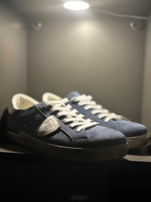 Blå Philippe Model sneakers i mocka - Snygga blå sneakers från Philippe Model i mjuk mocka med vita detaljer och vita skosnören. Klassisk låg modell med logotyp på sidan och bekväm innersula. Perfekta för dig som gillar stilrena och trendiga skor.