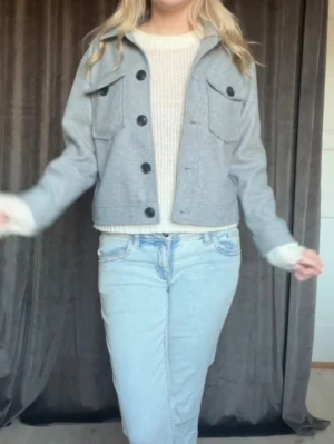 Grå overshirt med stora fickor - Snygg grå overshirt med stora svarta knappar och två bröstfickor med lock. Rak passform och klassisk krage. Perfekt att slänga över en tröja för en avslappnad look. Materialet ser ut att vara mjukt och lite tjockare, troligen ullblandning.