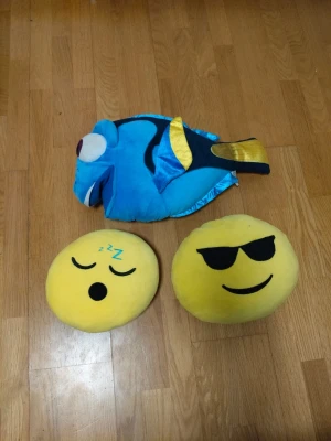 Gosedjur: Dory & emoji-kuddar - Tre mjuka gosedjur: en blå och gul fisk som liknar Dory från Hitta Nemo samt två runda gula emoji-kuddar, en med solglasögon och en sovande med Zzz. Perfekta som dekoration eller mysiga kuddar till soffan eller sängen.