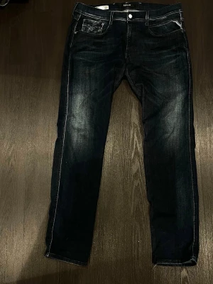 Mörkblå raka jeans från Replay - Säljer ett par mörkblå jeans från Replay med raka ben och klassisk femficksmodell. De är i storleken 36/34. Jeansen har snygga slitningar och kontrastsömmar, samt metallknappar och dragkedja. Materialet är denim i bomull med en skön passform. Vid minsta fundering är det bara att höra av sig🙂