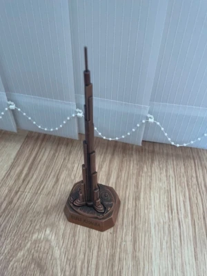 Burj Khalifa souvenir i metall - Säljer en brunfärgad miniatyr av Burj Khalifa i metall med detaljerad design och texten 'Burj Khalifa' samt 'Dubai' på basen. Perfekt som prydnad eller samlarobjekt för dig som gillar resor och arkitektur.