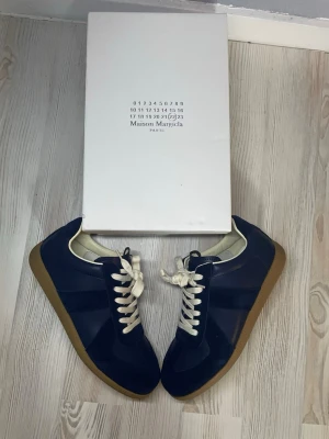 Gats - Snygga sneakers från Maison Margiela i mörkblått läder och mocka med vita skosnören och beige gummisula. Klassisk low-top siluett som passar perfekt till streetwear och casual outfits. Diskret branding och stilren design.