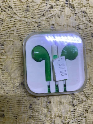 Gröna in-ear hörlurar i plastfodral - Snygga gröna in-ear hörlurar med vit sladd, levereras i ett genomskinligt plastfodral. Hörlurarna har en klassisk rundad form och passar perfekt till mobilen eller datorn. Materialet är plast och designen är enkel men stilren.