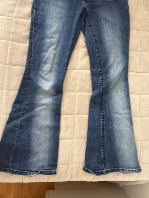 Blå bootcut jeans med slitningar - Säljer ett par blå bootcut jeans med snygga slitningar och tvättade detaljer från Ginatricot 14+