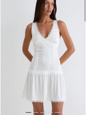 Vit nattlinne med spetsdetaljer - Säljer en vit kort klänning med v-ringad hals och fina spets/broderi detaljer. Klänningen är helt ny med prislapp kvar. 