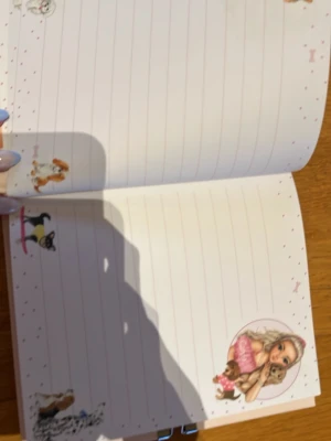 Top Model dagbok med hundmotiv - Söt dagbok från Top Model med ljusrosa omslag dekorerat med olika hundar och guldiga ben. Inuti finns linjerade sidor med hundillustrationer och en Top Model-figur. Dagboken har ett metallås för extra säkerhet.