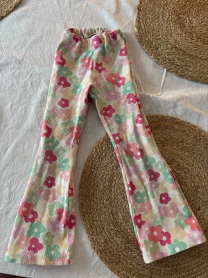 Blommiga utsvängda leggings - Supersöta leggings med utsvängda ben och färgglatt blommönster i rosa, grönt, gult och vitt. Tillverkade i ribbad stretchig trikå som sitter skönt. Storlek 104