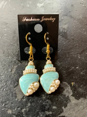 Turkosa snäckformade örhängen med pärlor - Unika örhängen i snäckform med turkos marmorerad yta, dekorerade med små vita pärlor och guldfärgade detaljer. Perfekta för dig som vill sticka ut med en cool accessoar. Krokar i guldfärg för enkel användning.