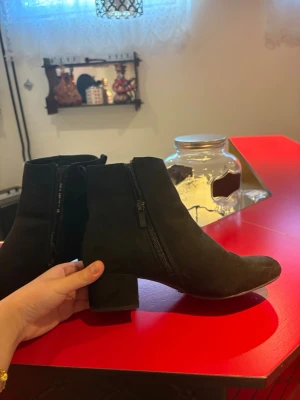 Svarta mockastövletter med klack - Snygga svarta stövletter i mocka-look med dragkedja på sidan och bred klack. Klassisk och stilren design som passar till många outfits. Skorna har en rundad tå och är perfekta för dig som gillar enkel men trendig stil.