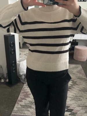 Beige stickad tröja med svarta ränder - Snygg stickad tröja i beige med svarta horisontella ränder. Tröjan har rund halsringning, långa ärmar och ribbstickade muddar vid ärmslut och nederkant. Perfekt för en avslappnad och trendig look.