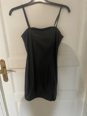 Svart kort skinklänning från H&M Divided - Svart kort skinklänning från H&M Divided med smala axelband och slits nertill. Enkel och stilren design som sitter snyggt på kroppen.