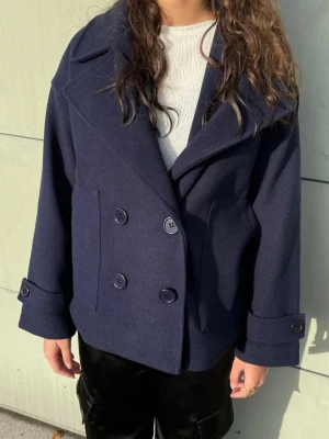 Mörkblå kappa från design by si - Säljer en mörkblå rkappa med bred krage och dubbelknäppning. Kappan har stora knappar framtill och på ärmsluten. Inga defekter. Storlek Xs/S