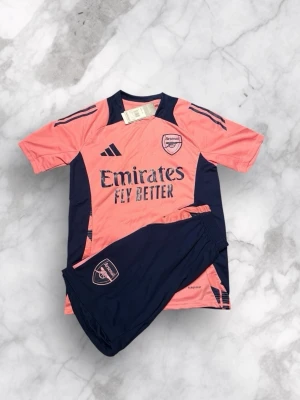 Football Kit Adidas Arsenal 2023  - This is an Adidas Arsenal football kit in pink and navy blue. The kit includes a jersey and shorts, both featuring the Arsenal logo and sponsor branding.  ⭐️ Condition: 10/10 🎨 Color: Pink and Navy Blue 📦 Fast and careful shipping