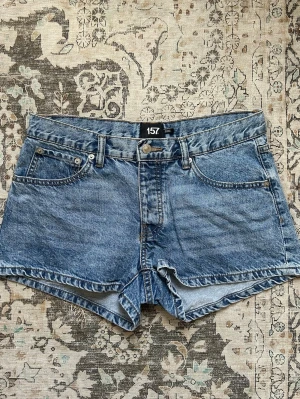Blå denimshorts från 157 med brodyr - Snygga blå denimshorts från 157 med klassisk femficksdesign och broderade detaljer på bakfickorna. Shortsen har normal passform för en avslappnad look. Perfekta för varma sommardagar.