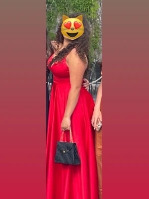 Röd långklänning med v-ringning - Elegant röd långklänning med djup v-ringning och smala axelband. Klänningen har en figurnära överdel och ett utsvängt kjolparti som ger en klassisk siluett. Perfekt för bal eller festliga tillfällen. Klänningen är i storlek 38 men den är lite små i storleken, (ungefär 36-38). Original priset är 3000kr då vi köpte den från en butik, den har endast blivit använd EN gång. 