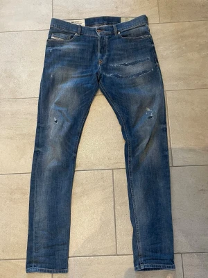 Blå diesel med slitningar - Säljer ett par blå skinny jeans med slitningar och lätt tvättad look. Jeansen har klassisk femficksmodell och dragkedjegylf. Perfekta för en avslappnad och trendig stil. 30/32