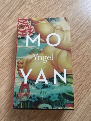 Yngel av Mo Yan - Romanen 'Yngel' av Mo Yan har ett färgstarkt omslag med konstnärlig illustration av ett barn och blommor. Boken är tryckt i pocketformat och har tydlig vit text på framsidan. Perfekt för dig som gillar modern skönlitteratur och prisbelönta författare.