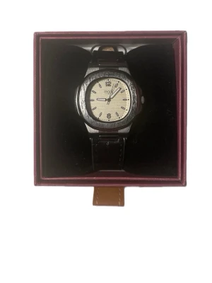 Regal Klocka - Stilren klocka från TKO med svart läderband och rund urtavla i silver och vitt. Klockan har tydliga siffror och klassisk design, perfekt för dig som gillar en tidlös accessoar. Levereras i originalask.