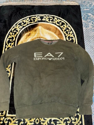 Mörkgrön EA7 Emporio Armani sweatshirt - Snygg mörkgrön sweatshirt från EA7 Emporio Armani med tryckt logga på bröstet. Tröjan har rund halsringning, långa ärmar och ribbade muddar vid ärmslut och nederkant. Perfekt för en avslappnad och trendig stil. Pris går att diskutera