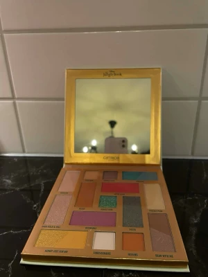 The Jungle Book ögonskuggspalett - Säljer en ögonskuggspalett från Catrice x Disney The Jungle Book med spegel. Paletten innehåller flera färgstarka och neutrala nyanser i både matta och skimrande toner, inklusive grönt, lila, guld, orange och beige. Förpackningen har motiv av Mowgli och Hathi Jr.