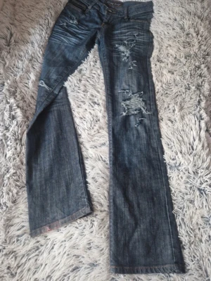 Blå slitna bootcut vintage jeans  - Säljer dessa så snygga vintage jeans med coola slitningar då de tyvärr inte passar mig. Midjemåttet är 35 cm rakt över, innerbenslängden är 80 cm och grenmåttet är ca 18cm. De är lite missfärgade längst ner vilket syns på sista bilden 