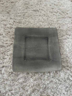 Grå fyrkantig tallrik Mateus - Säljer en stilren fyrkantig tallrik från Mateus i grått porslin. Tallriken har en matt finish och modern design med mjukt rundade hörn. Perfekt för dig som gillar minimalistisk och snygg dukning.