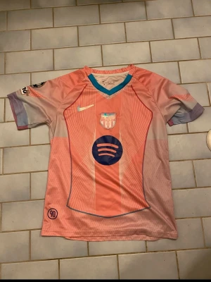 Barça matchtröja rosa Nike - Säljer en FC Barcelona matchtröja i rosa och ljuslila med blå detaljer. Tröjan har klubbmärke, Nike-logga och Spotify som sponsor på bröstet. Korta ärmar och V-ringad krage med blå kant. Perfekt för fotbollsträning eller att bära som supporter.