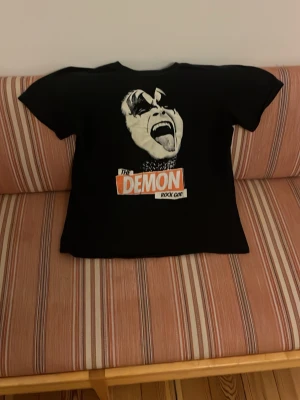 Svart The Demon Rock God t-shirt - Cool svart t-shirt med tryck av The Demon Rock God på bröstet. T-shirten har korta ärmar och en klassisk passform. Perfekt för dig som gillar rock och vill sticka ut med en unik grafisk design.