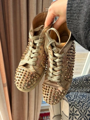 Christian Louboutin Flat Spike - Guldiga Christian Louboutin Flat Spike skor! (Med inslag av rosé). Kom gärna med bud!!! Väl använda med har mycket kvar att ge! Köpta på Vestiaire Collective med äkthets garanti men eftersom jag köpt dem second hand själv så har jag inga äkthetsbevis/låda/dustbag- därav det lägre priset. Nya vita skosnören kan skickas med vid förfrågan!
