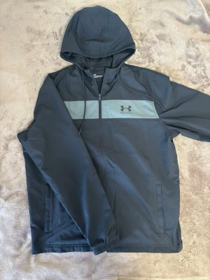 Svart Under Armour Jacka - Snygg svart vindjacka från Under Armour. Riktigt snygg nu inför våren. Använd fåtal gånger - bra skick.