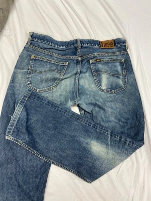Lee jeans  - Säljer ett par klassiska blå jeans från Lee med raka ben och snygga slitningar. Jeansen har fem fickor, normalhög midja och Lee-logga på bakfickan. Perfekta för en avslappnad och trendig stil.