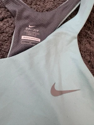 Mintgrön  träningstopp från Nike - Snygg ljusblå träningstopp från Nike med grått meshfoder och klassisk Dri-FIT-teknologi. Toppen har brottarrygg och ett diskret Nike Swoosh på bröstet. Perfekt för gymmet eller löprundan.