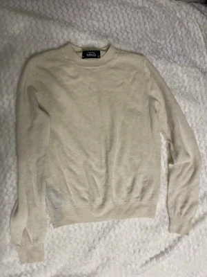 Beige stickad tröja från MNG - Klassisk beige stickad tröja från MNG med rund halsringning och långa ärmar. Tröjan har en enkel och stilren design med ribbade muddar vid ärmslut och nederkant. Perfekt att matcha med jeans eller kjol för en avslappnad look.