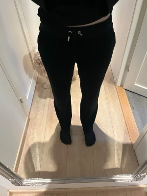 Svarta Juicy Couture mjukisbyxor - Säljer ett par svarta mjukisbyxor från Juicy Couture med dragsko i midjan och fickor. På baksidan finns texten 'Juicy' i glittriga stenar som ger en snygg och trendig look. Perfekta för en chill och avslappnad stil.