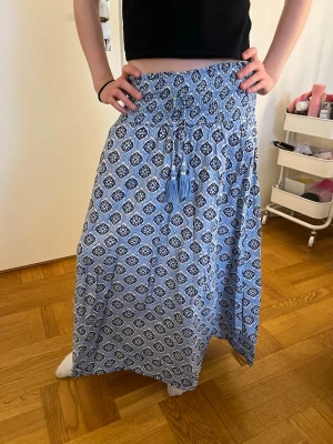 Blå mönstrad långkjol - Säljer en blå långkjol med vitt och svart mönster. Tänk dig den med typ en fin kofta eller nåt på sommaren