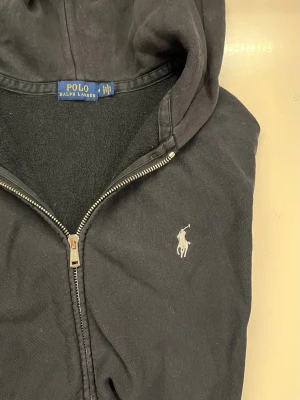 Svart zip hoodie från Polo Ralph Lauren - Klassisk svart hoodie med dragkedja från Polo Ralph Lauren. Tröjan har huva och två fickor framtill. Storlek M men sitter som en S. hör av dig för fler bilder. Priset är inte hugget i sten 🪨. 😊👒✌️