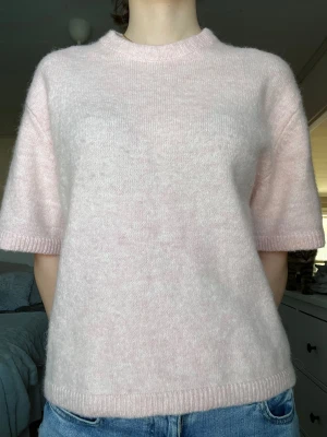 Ljusrosa stickad t-shirt - Ljusrosa stickad t-shirt från Gina Tricot i storlek S. Tröjan har korta armar / trekvartsärmar och rund hals. Tröjan har en avslappnad passform och ribbade kanter vid ärmslut, hals och nederkant. 