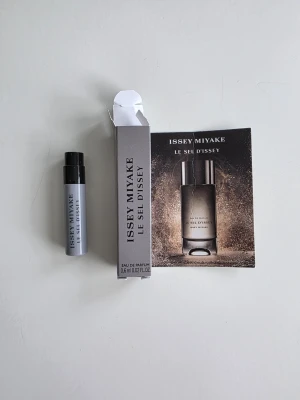 Issey Miyake Le Sel d'Issey Eau de Parfume - Parfymprov på Le Sel d'Issey från Issey Miyake. Provet är i en liten cylinderformad flaska på 0,6 ml med svart lock. Doften har marina och träiga toner med inslag av salt, rökelse och amberträ. Förpackningen är grå och elegant.