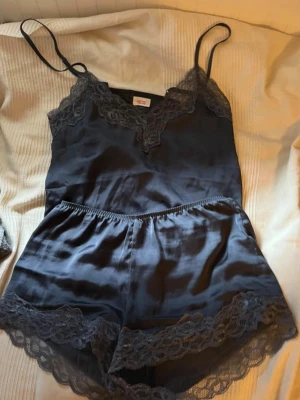 Marinblå setinset med tunna axelband - Snyggt set som är marinblått från H&M med tunna axelband och v-ringning. Set kommer i shorts och ett linne och  har fina spetsdetaljer vid halsringning och benslut samt är gjord i ett glansigt, mjukt material som känns lyxigt mot huden. Perfekt för dig som gillar en stilren och feminin look.