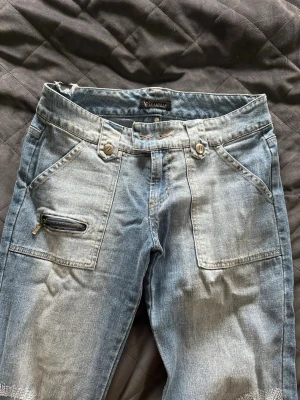 Ljusblå bootcut jeans  - Snygga ljusblå bootcut jeans med dragkedjedetalj på ena fickan och markerade sömmar. Jeansen har två framfickor och vida ben, perfekt för en avslappnad och trendig look. Tillverkade i klassisk denim. Kapparna vid midjan är borta men har en och kan skicka med, men tycker de funkar utan med en längre tröja eller säkerhetsnål! Kan även sy dit nya knappar 💕