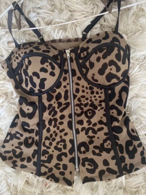 Leopardmönstrad korsett med dragkedja - Snygg korsettopp med leopardmönster i beige och svart. Toppen har smala axelband, markerade kupor och en dragkedja framtill. Perfekt för dig som vill sticka ut med en trendig och edgy look.
