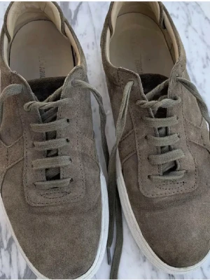 Arigatos - Snygga sneakers från Arkk i grågrön mocka med vita sulor. Klassisk låg modell med rund tå och matchande skosnören. Perfekta för dig som gillar stilrena och minimalistiska skor med en modern touch.
