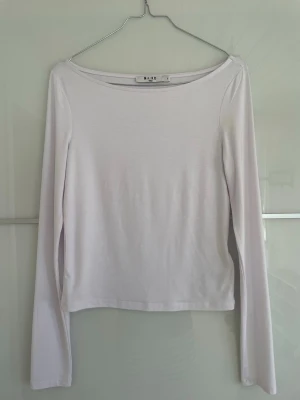 Vit långärmad topp från NA-KD - En enkel och stilren vit långärmad topp från NA-KD. Toppen har en boatneck urringning och är tillverkad i ett mjukt material som känns skönt mot huden. Perfekt att matcha med jeans eller kjol för en clean look.