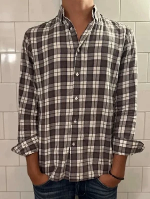 Flanell skjorta från Massimo Dutti - Snygg rutig flanellskjorta från Massimo Dutti i brunt och vitt. Skjortan har klassisk krage, knäppning framtill och långa ärmar. Tillverkad i mjuk bomull, perfekt för en avslappnad men stilren look.