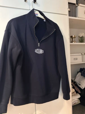 Svart halfzip från Jack & Jones - Snygg svart halfzip-tröja från Jack & Jones med dragkedja framtill och broderad logga på bröstet. Tröjan har hög krage och är tillverkad i mjukt sweatshirtmaterial. Perfekt för en chill och stilren look.